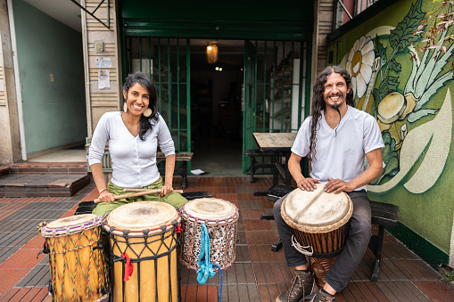 Portrait of friends playing djembe drum outdoors
