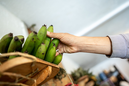 Close-up of a hand picking unripe bananas at market
