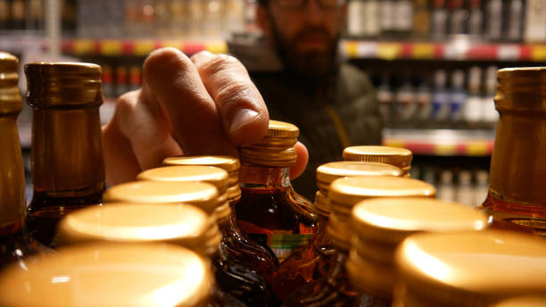 Close-up of many luxury bottles of cognac in a department store and a male buyer takes one stock photo