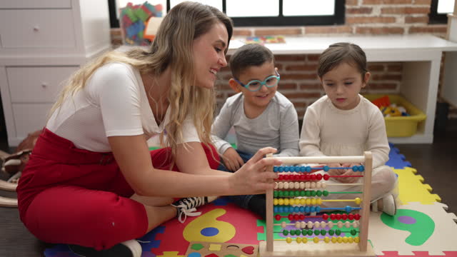 Teacher with boy and girl learning maths with abacus sitting on floor at kindergarten