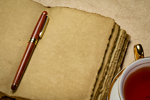 blank retro leather-bound journal with decked edge handmade paper pages with a stylish pen and a cup of tea, journaling concept