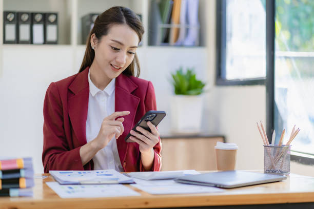 istock Pretty successful Asian businesswoman using smartphone and working on laptop while sitting at desk checking monthly account and spending in company 1480602526