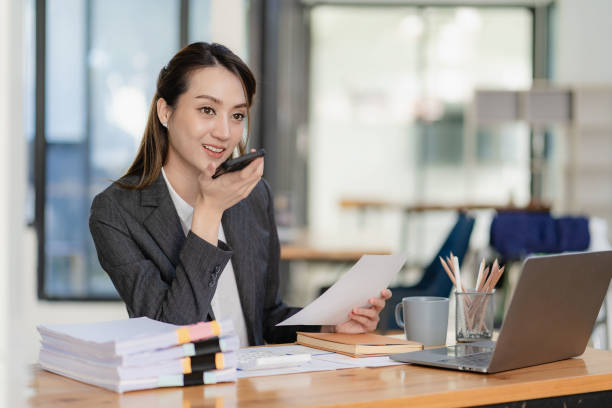istock Pretty successful Asian businesswoman using smartphone and working on laptop while sitting at desk checking monthly account and spending in company 1480602626
