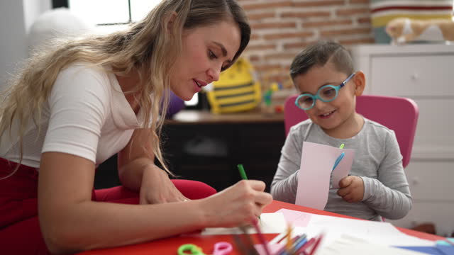 Teacher and toddler sitting on table having handcrafts class at kindergarten