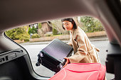 istock Young woman putting a suitcase in a back of a car 1480607024