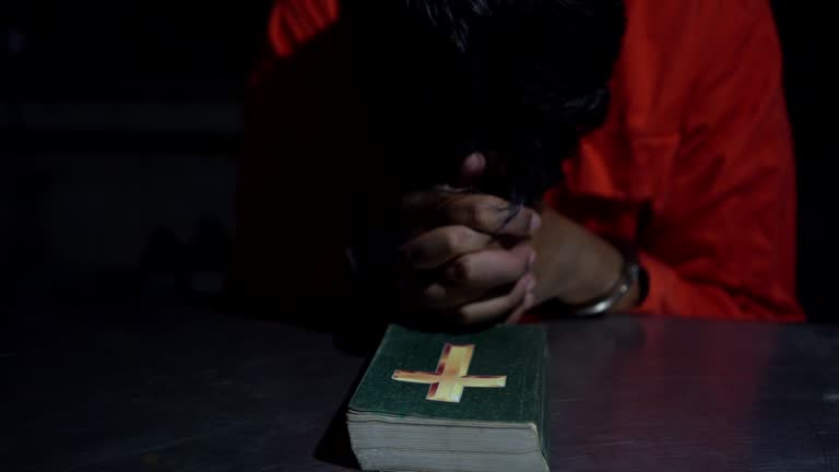 Prisoner in handcuffs reading holy bible in cell