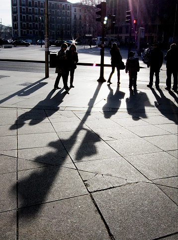 People standing,waiting to cross the street, their shadows and traffic light in the foreground on paving stone. Madrid, Spain.