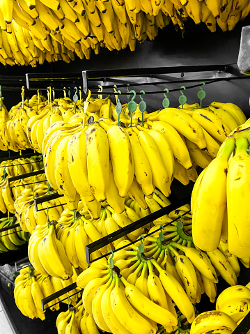Bananas displayed in a supermarket near the fruit area. Mention product display and creative visual merchandising for everyday products that are inexpensive but great for health.