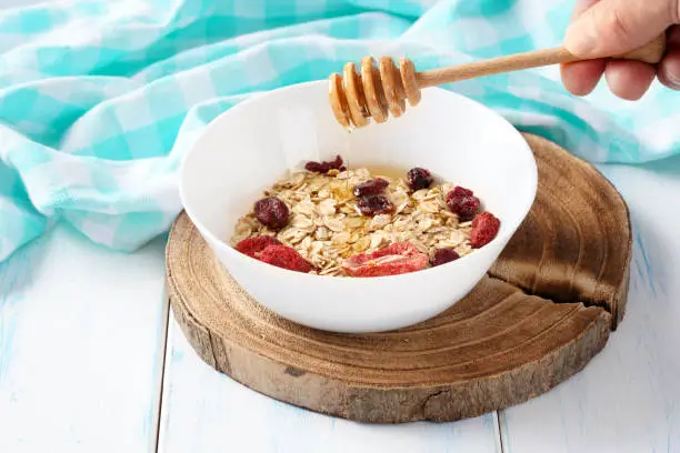Oat grain cereal with berries and honey in a white plate on a wooden table.