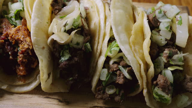 Authentic street tacos feature tender carne asada on soft corn tortillas, topped with cheese, fresh lime, and chopped cilantro and onion, on a rustic wood cutting board.