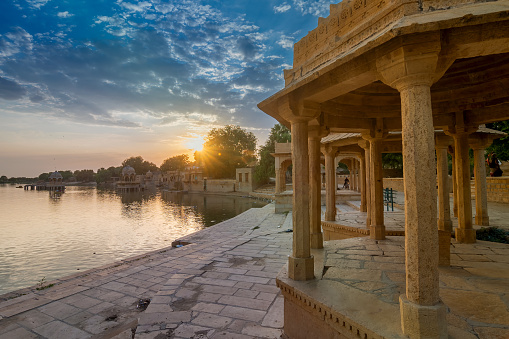 Chhatris and shrines of hindu Gods and goddesses at Gadisar lake, Jaisalmer, Rajasthan, India. Indo-Islamic architecture , sun set and colorful clouds in the sky with view of the Gadisar lake.