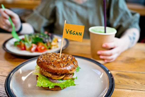 Woman eating veggie salad and  burger with "Vegan" word on small flag   in a veggie restaurant or food court stock photo