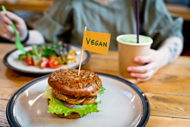 fotografii de stoc, fotografii și imagini scutite de redevențe cu femeie mananca salata veggie si burger cu "vegan" cuvânt pe steag mic într-un restaurant veggie sau food court - aliment vegan
