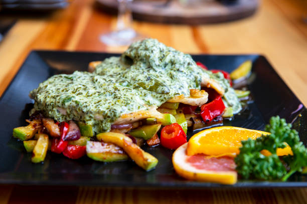 Spinach sauce on Grilled Chicken Breasts with roasted vegetables. Tuscan Chicken in a Creamy Spinach Sauce with tomatoes and zucchini served on black plate with fresh orange slices. Close up