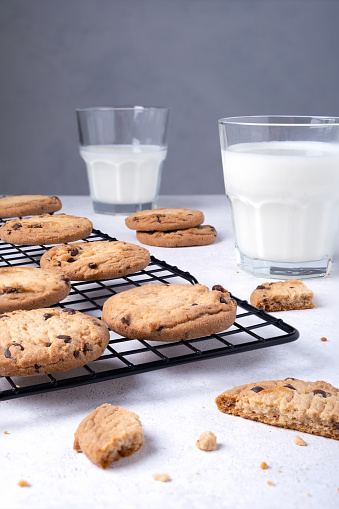 Close-up of baked oatmeal cookies with chocolate chips on a metal cooling rack and milk in a glass. Selective focus. Vertical orientation.