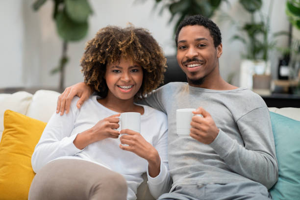 istock Cute african couple posing on couch at home, drinking coffee 1480645328
