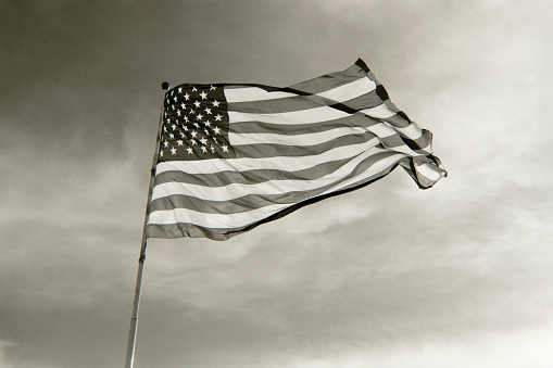 A black and white 35mm film scan of a backlit American Flag waving in the wind.