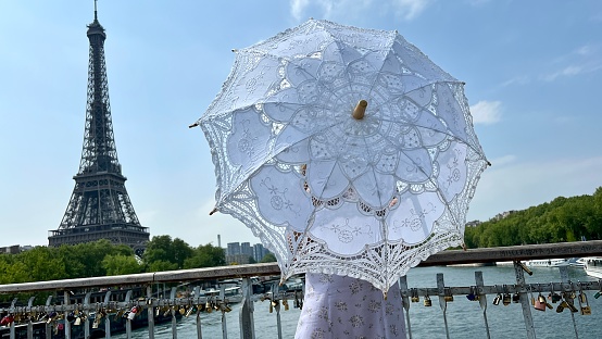 a girl with a white parasol stands against the backdrop of the Eiffel Tower with her back to us can be used for advertising for the Internet for travel agencies. High quality photo