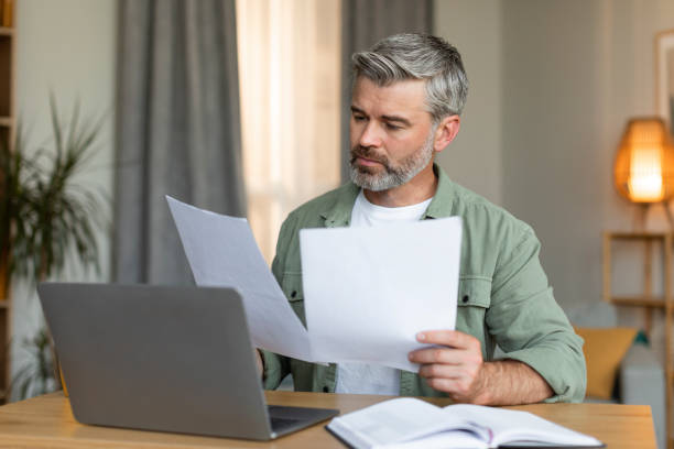 istock Serious busy old caucasian man manager works with documents, sits at table with computer in living room 1480645810