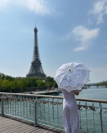 a girl with a white parasol stands against the backdrop of the Eiffel Tower with her back to us can be used for advertising for the Internet for travel agencies. High quality photo