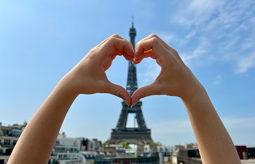 a man shows a heart with his hands connecting his fingers on the background of the Eiffel Tower. High quality photo