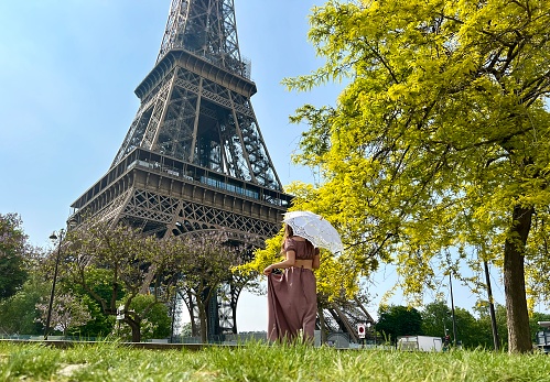 a beautiful girl in a long dress stands against the blue sky and the Eiffel Tower in a restaurant. She looks into the frame there is a place for advertising travel agency. High quality photo