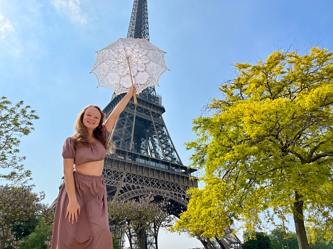 a girl with a white parasol stands against the backdrop of the Eiffel Tower with her back to us can be used for advertising for the Internet for travel agencies. High quality photo