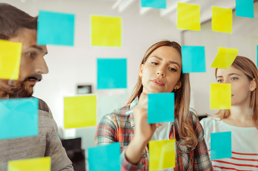 Shot of Coworkers Using Sticky Notes on a Glass Wall During a Meeting