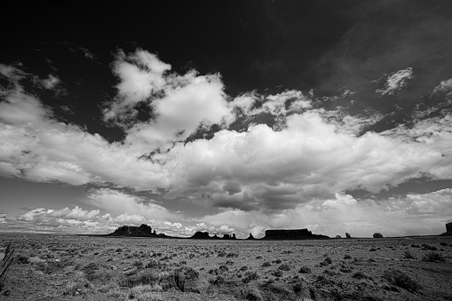 Black and White Monument Valley's iconic Navajo Mittens rise from the desert floor, contrasting against a dramatic cloudscape. This stunning landscape spans the border of Utah and Arizona