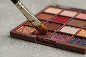 Colorful eyeshadow palette with brush on grey table, closeup view