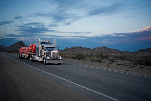 Semi-truck makes its way across the Arizona desert at dusk, the silhouette of its flatbed against the vibrant sky as it traverses the open road
