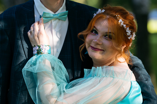 Young redhead bride in blue dress touching groom's bow-tie. Candid photo of young couple of newlyweds. Wedding or prom photo.