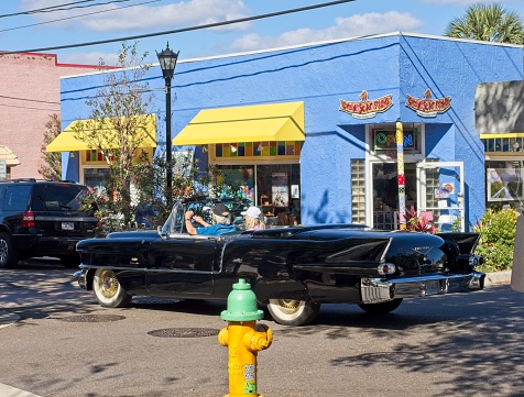 Los Angeles, CA, USA – August 21, 2022: General shot of people at Lowrider event displaying lowriders on three wheels parked outdoors with local business in the background taken from behind cars  in southern California