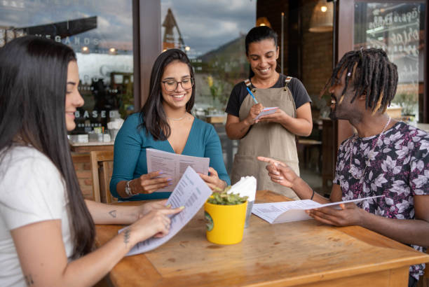 amici sorridenti che danno un ordine a un server mentre sono seduti al bar sul marciapiede - cafe coffee shop sidewalk cafe menu foto e immagini stock