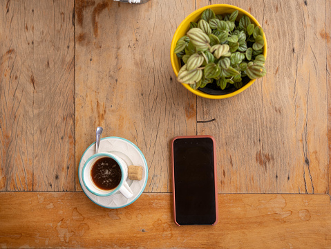 High angle view of a mobile phone sitting on a table next to a cup of coffee and a potted plant at a cafe