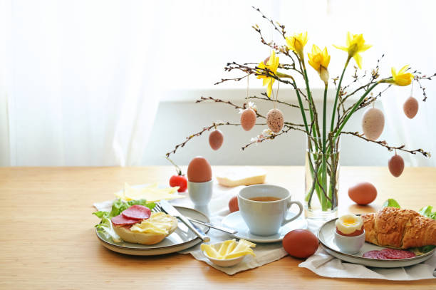 istock Easter breakfast served on a wooden table with a bouquet from daffodil flowers, spring branches and hanging egg decoration, copy space, selected focus 1480663378