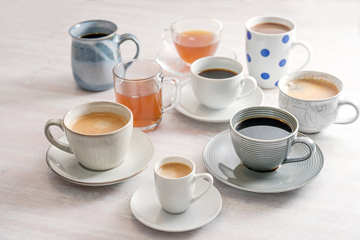 Group of different cups and mugs with coffee and tea drinks on a light table,  selected focus, narrow depth of field
