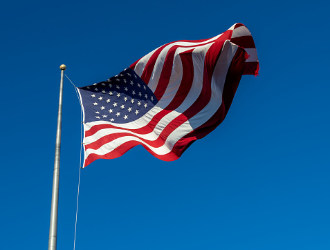 This image shows a close-up view of an American flag waving on a flagpole, with blue sky background.
