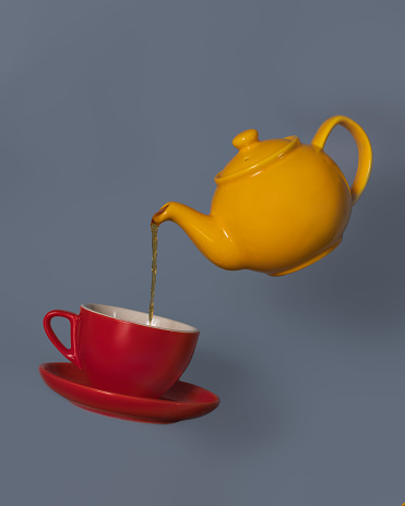 A yellow teapot levitating and pouring tea to a red cup. Conceptual food photography