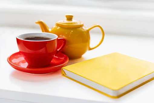 Morning tea in a red tea cup and a yellow teapot, and a yellow journal captured in natural light