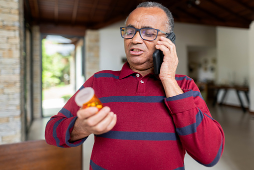 Senior man standing in his living room and calling his pharmacy for advice on his medication dose