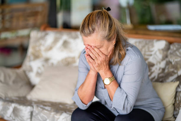 Senior woman with depression sitting with her head in her hands at home Depressed senior woman sitting alone with her head in her hands on a living room sofa at home senior women stock pictures, royalty-free photos & images