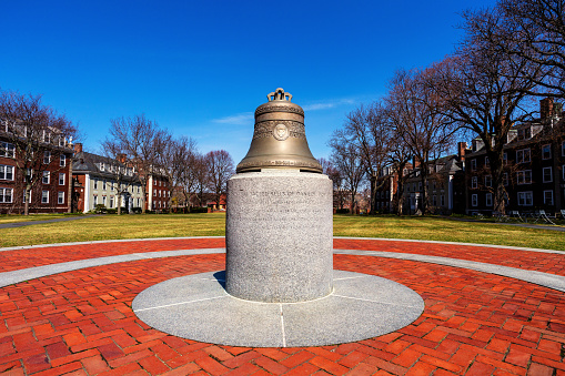 Boston, Massachusetts, USA - March 31, 2023: Wide angle view of the half-size replica of the Centennial Bell (1908-2008) on display in front of the Baker Library of the Harvard Business School (HBS) . The actual Centennial Bell is atop the library building. View looking in the direction of the Charles River.