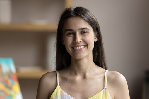 Happy beautiful young Hispanic artist girl standing in creative studio, looking at camera, smiling, laughing. Cheerful pretty art school student head shot front portrait