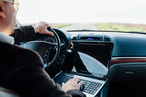 Business man using laptop while driving car