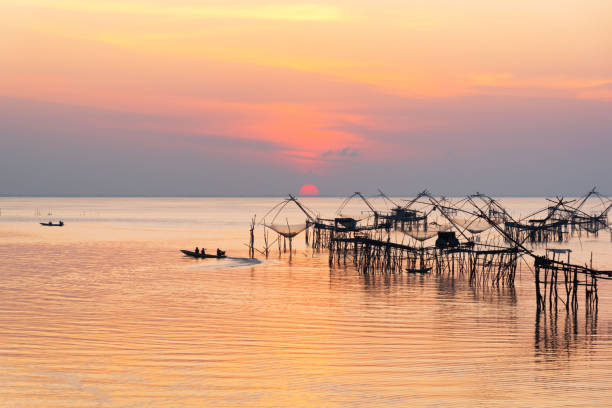 Scene of sunrise and tourist visiting giant fishing net Sunrise and silhouette image of tourists on long tail boat and giant fishing net in the morning at Pakpra, Phatthalung, Thailand. phatthalung province stock pictures, royalty-free photos & images