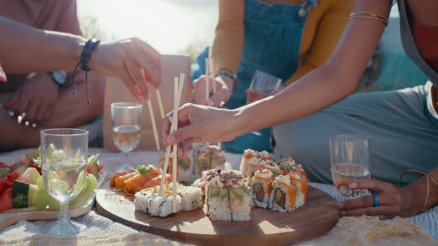 Sushi picnic, chopsticks or hands of people bonding or eating outdoors together on grass or holiday vacation. Closeup, food or healthy friends love relaxing or drinking water in summer on park dates