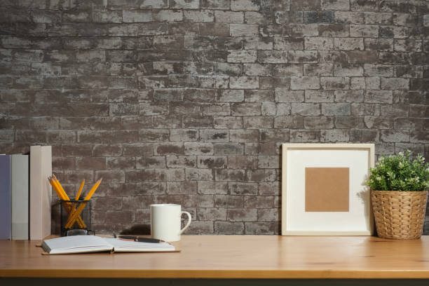 Blank picture frame, coffee cup, notebook and potted plant on wooden table. Stylish working space, home office.