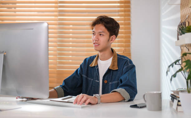 istock Smiling young asian man looking at computer screen, working online or browsing internet website. 1480708630