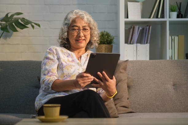 istock Pleasant modern senior woman relaxing on sofa at cozy home and using digital tablet. Elderly technology concept. 1480710150